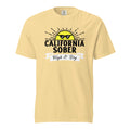 A yellow t-shirt with an illustration of a sun with shades on with the caption, "California Sober: High & Dry".